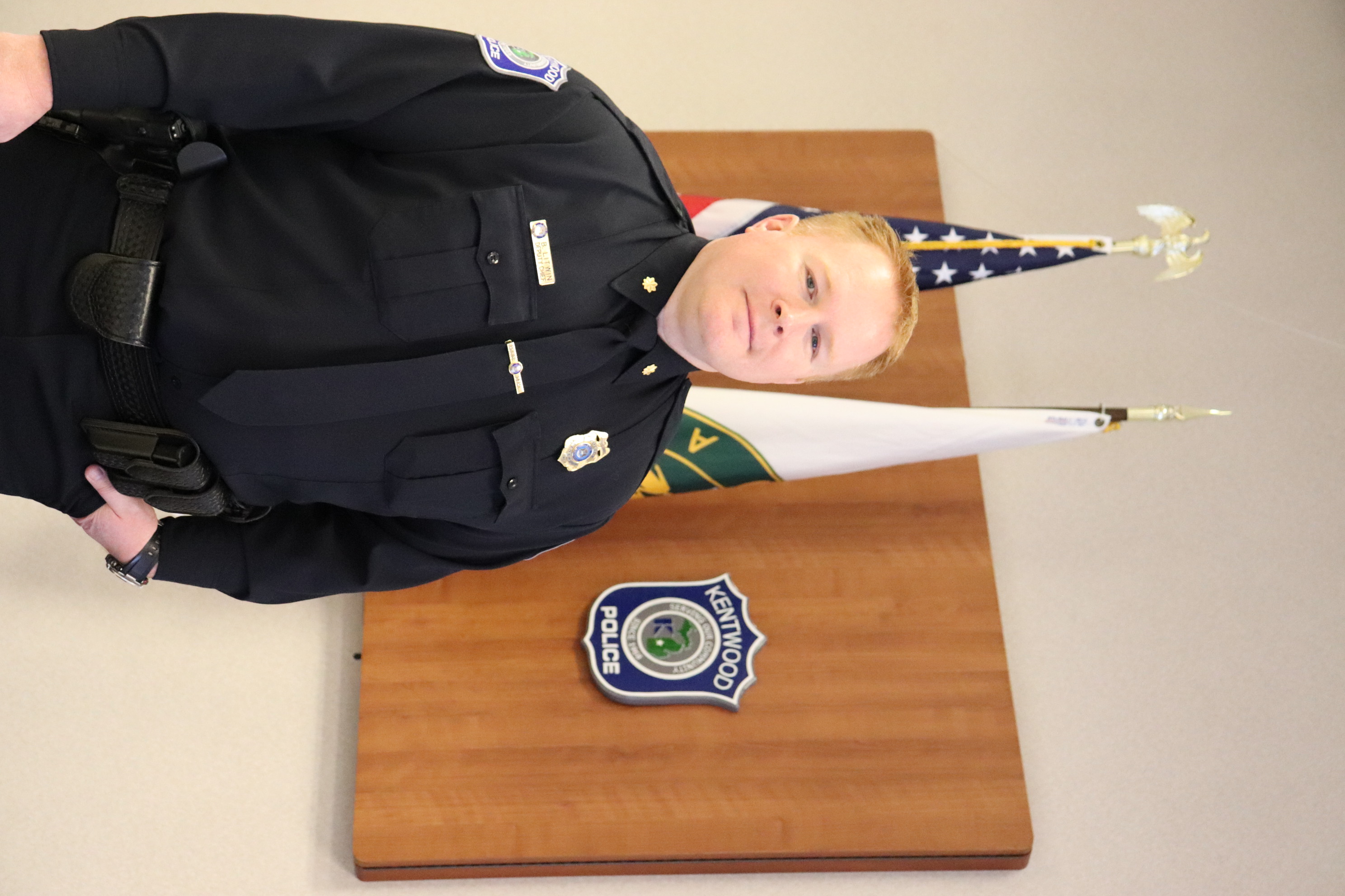 Bryan Litwin in front of the American and City of Kentwood flags and the Kentwood Police Department Patch